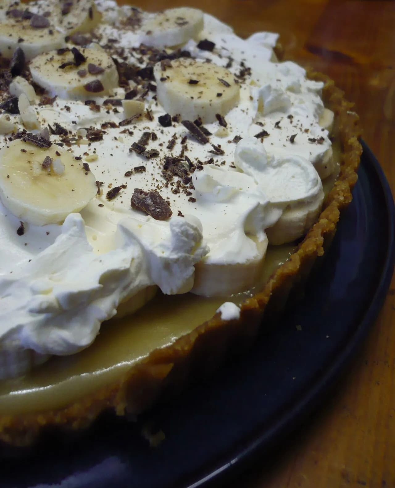 Foto da receita: Banoffee (Torta de Banana com Doce de Leite) - Base de biscoito amanteigado, camada de doce de leite, rodelas de banana e chantilly com cacau por cima. Torta gelada sem forno, montada em 30 minutos.