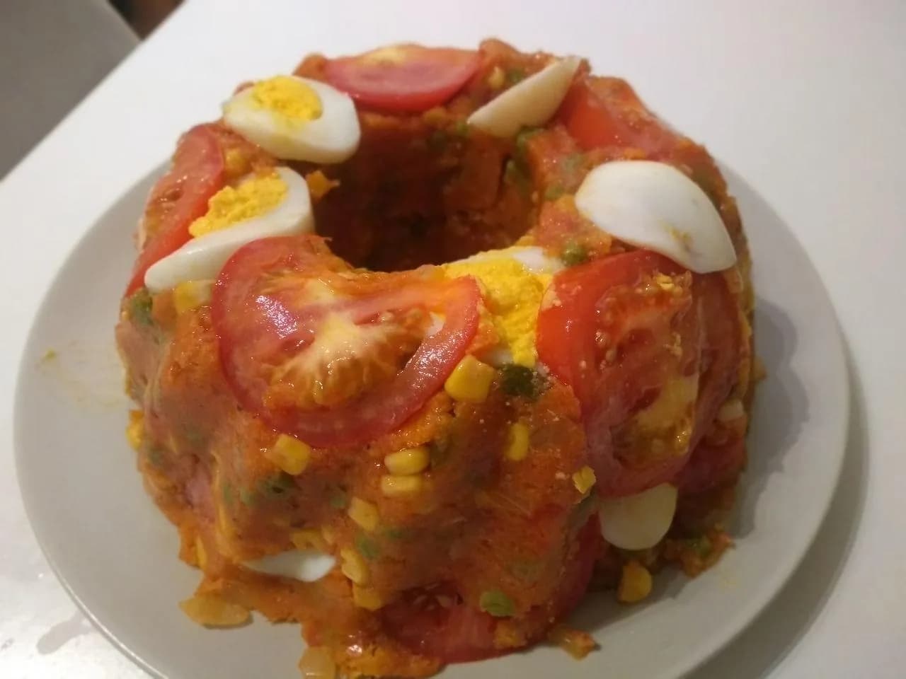 Foto da receita: Cuscuz Paulista - Farinha de milho cozida com molho de tomate, sardinha ou frango, palmito, ervilha e ovos, prensada em forma decorada e servida em fatias. O cuscuz de mesa de festa de São Paulo.