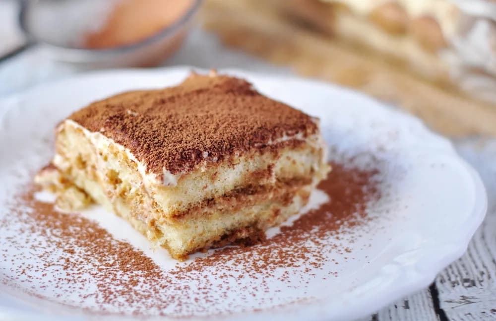 Foto da receita: Tiramisù Clássico - Camadas de biscoito champanhe embebido em café e creme de mascarpone com gemas, finalizado com cacau em pó. A sobremesa italiana mais pedida, sem forno.