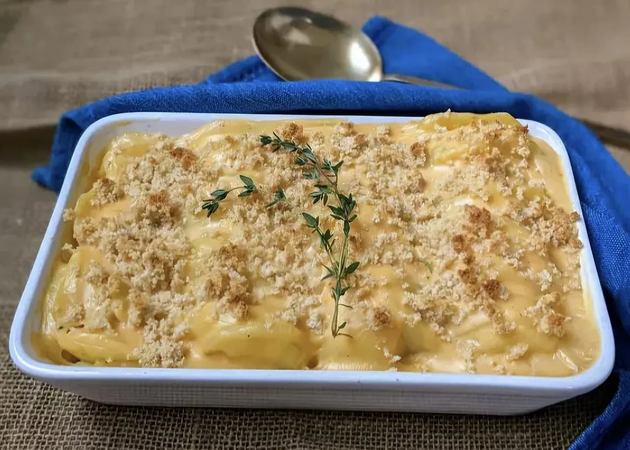 Foto da receita: Batata Gratinada com Creme de Leite - Fatias finas de batata assadas em camadas com creme de leite, alho, queijo e noz-moscada até ficarem macias e douradas. O acompanhamento de forno que rouba a cena.