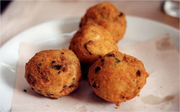 Foto da receita: Bolinho de Bacalhau Crocante - Bacalhau desfiado misturado com purê de batata e ervas, modelado em duas colheres e frito até dourar. Lanche de domingo na padaria.