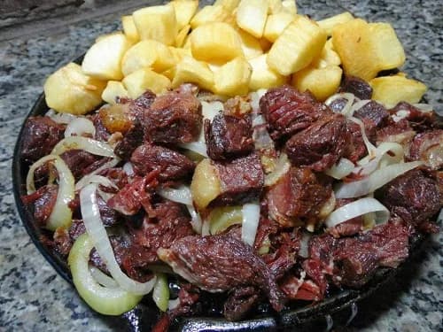 Foto da receita: Carne de Sol com Mandioca Frita - Carne salgada e seca ao sol, dourada na manteiga, servida com mandioca crocante e cebola roxa. Ícone dos restaurantes do Sertão.