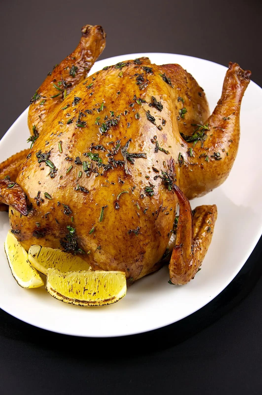 Foto da receita: Frango Assado com Batatas - Frango inteiro temperado com alho, limão e ervas, assado sobre batatas que douram na gordura da ave. O almoço de domingo em uma única assadeira.