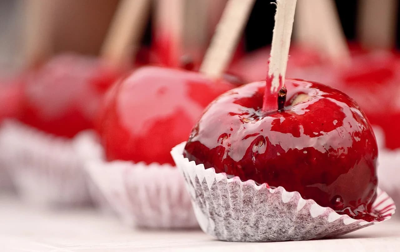Foto da receita: Maçã do Amor - Maçã inteira no palito coberta com calda de caramelo vermelho que endurece como vidro. O doce mais tradicional de festa junina e de parque de diversões.