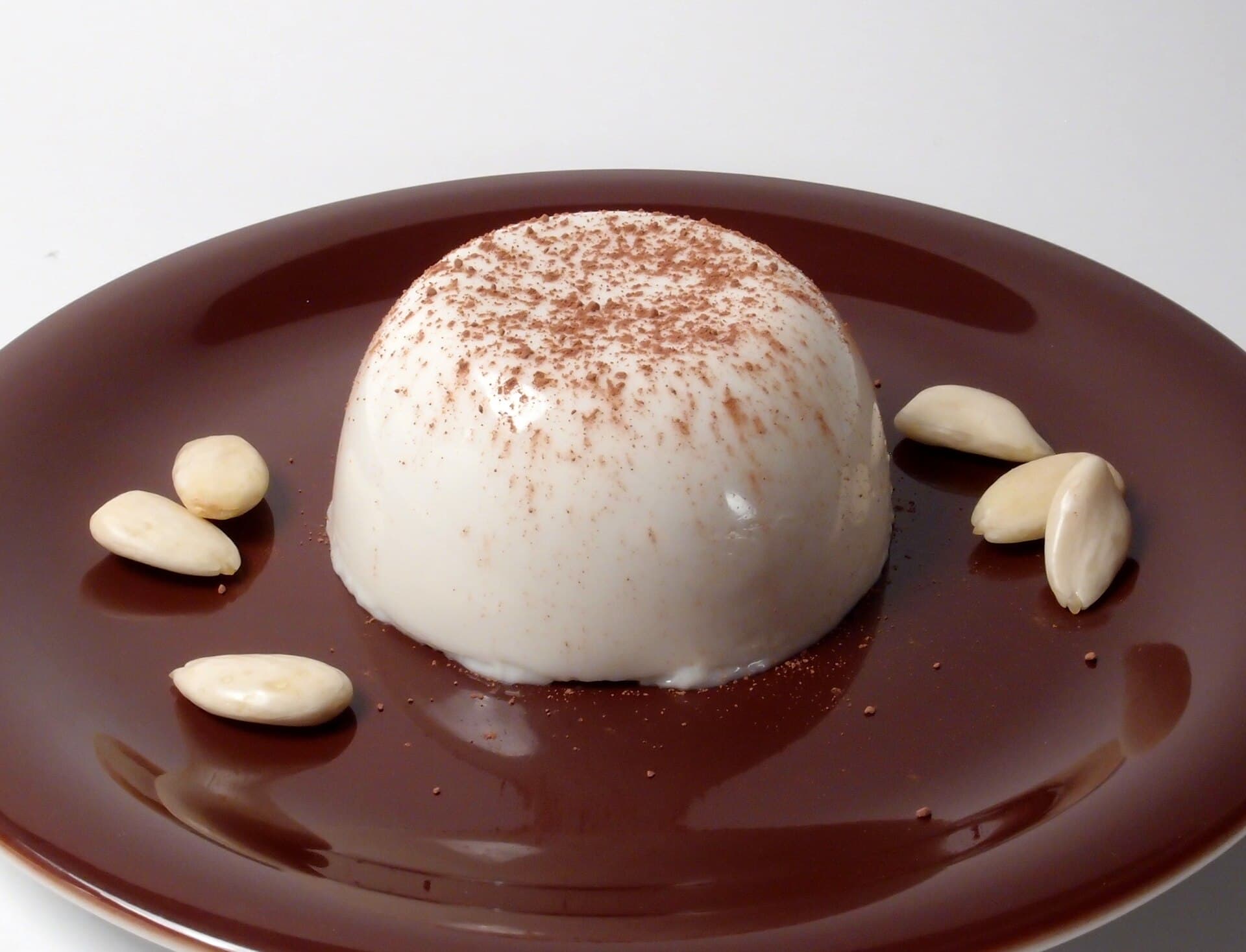 Foto da receita: Manjar Branco com Calda de Ameixa - Pudim branco perfumado com leite de coco, finalizado com calda escura de ameixa preta. Cremoso, leve, sobremesa de domingo.
